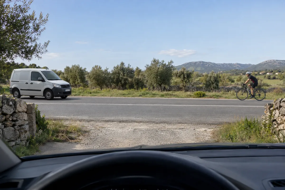 Desde un camino privado se ven una furgoneta por un lado de la vía y una bicicleta por el otro.