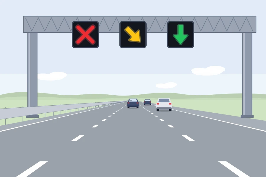 Pórtico con semáforos de carril: aspa roja sobre el carril izquierdo, flecha amarilla oblicua sobre el central y flecha verde hacia abajo sobre el derecho