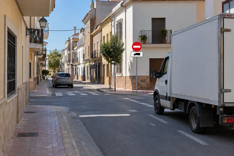 La señal de entrada prohibida con el panel de camiones debajo: un coche entra en la calle y un camión espera ante la señal