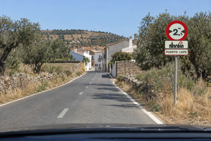 La entrada a un pueblo: la señal de limitación de anchura y el cartel con el nombre del poblado, en el mismo poste