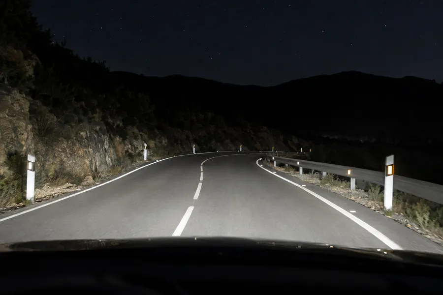 Una carretera de montaña de noche: los faros hacen brillar los hitos de arista del borde y los captafaros del trazado