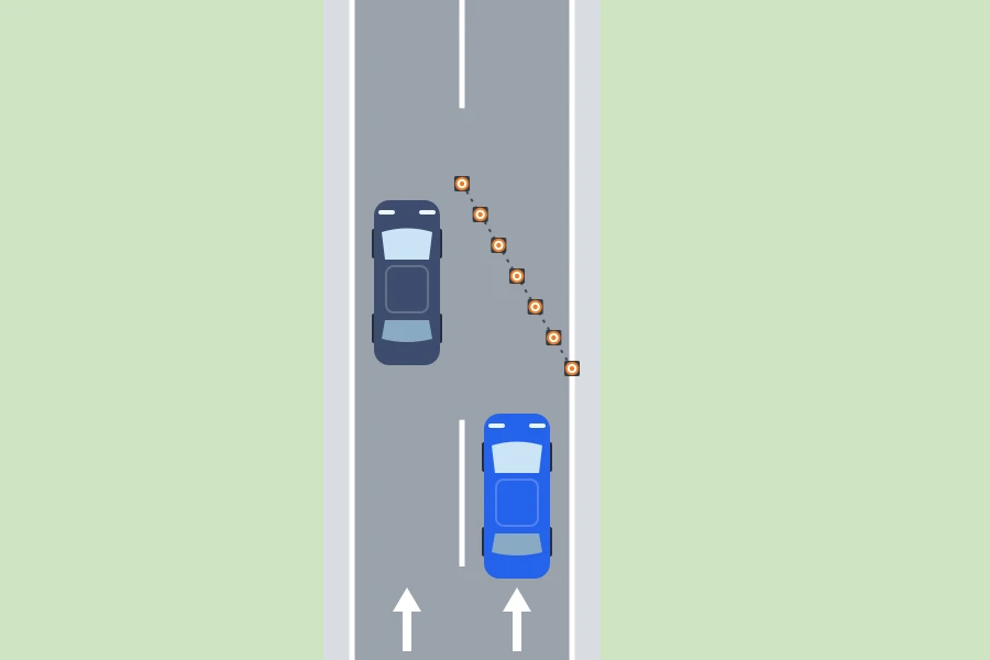 Esquema visto desde arriba: un coche azul espera ante una fila de conos en diagonal que cierra el carril derecho, unidos por una línea de puntos, mientras un coche gris pasa por el carril izquierdo abierto