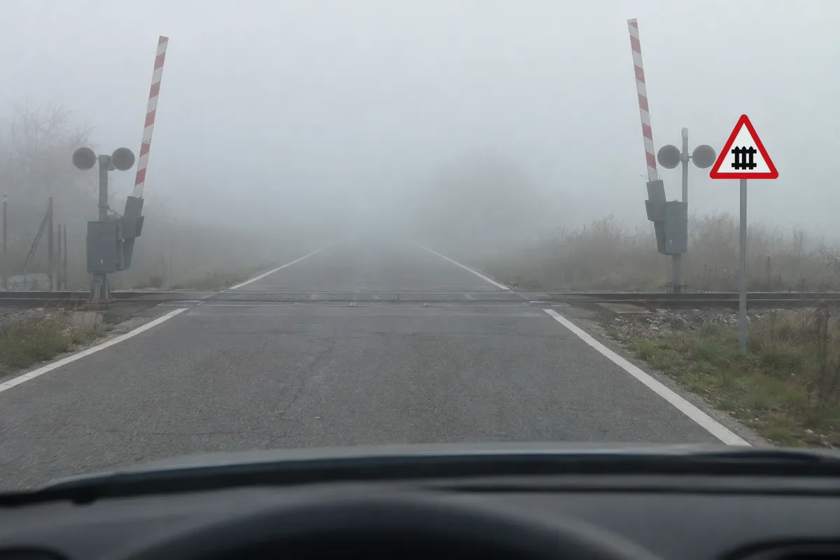 Niebla muy densa de día, al acercarse a un paso a nivel con la barrera levantada.