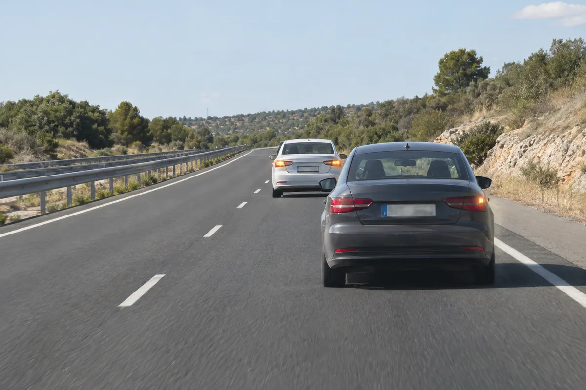 Un turismo sigue circulando por una autovía con las luces de emergencia y un coche detrás.